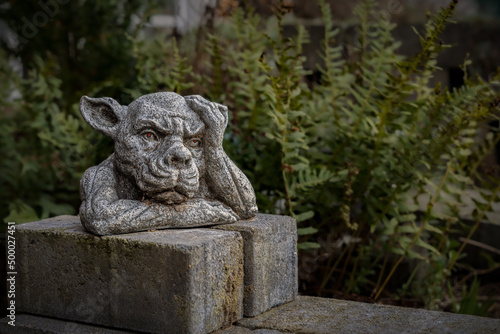 Closeup of a statue of a gargoyle or a gordon with its hand on the head in a park or garden