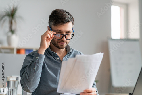 Busy mature male entrepreneur working with papers at workplace in office, checking financial reports