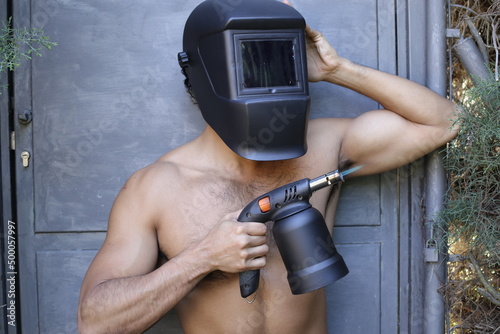 Shirtless welder holding a blowtorch