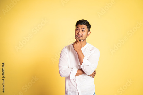 asian man glancing up with sarcastic expression with hand holding chin on isolated background