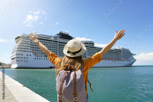 Back view of traveler girl with raised arms standing in front of big cruise liner