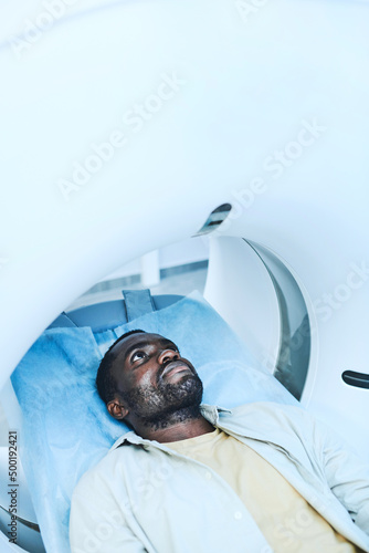 Serious young African-American patient with stubble lying on couchette of MRI machine while undergoing procedure