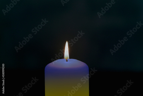 Płomień świecy w ciemnościach. Świeca ma zabarwienie niebiesko żółte, symbolizuje solidarność z Ukrainą.