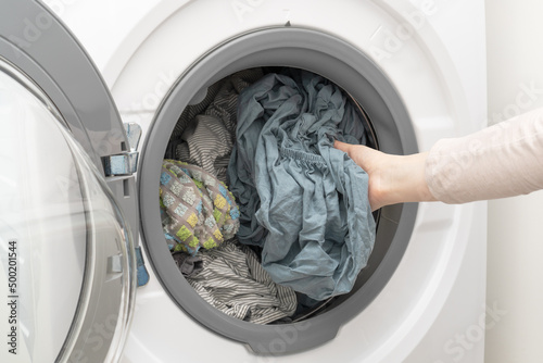 Clean wet laundry inside of washing machine. Woman's hand pulling out washed clothes from the drum.