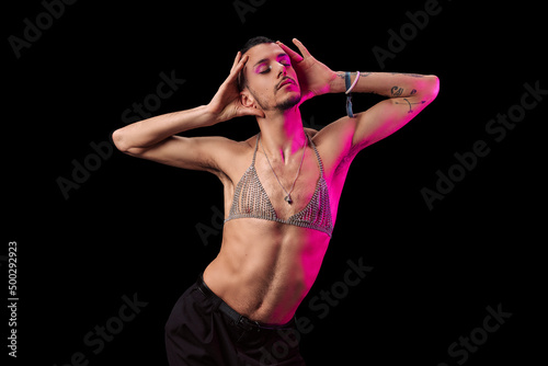 Young model with tattoos, shirtless and makeup. Posing with a black background and magenta light. Showing her feelings.