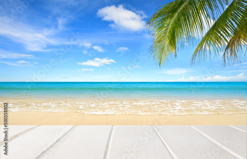 White wood board and palm leaves with beach and blue sky background.