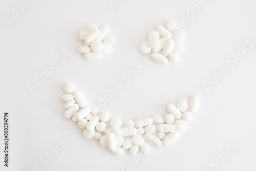 Białe lekarstwa i witaminy w tabletkach rozsypane na jasnym tle tworzą uśmiech, suplementacja diety, leczenie przewlekłe, farmacja,