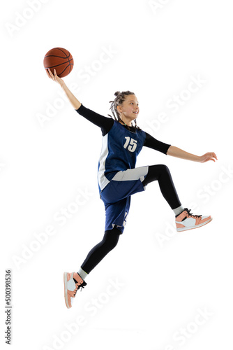 Portrait of teen girl in blue uniform training, playing basketball isolated over white background. Scoring winning goal