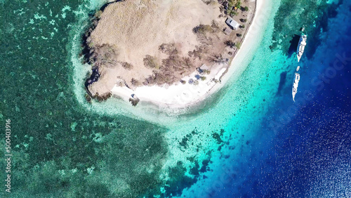 Top down drone shot of paradise island in Komodo National Park, Flores, Indonesia. The island has scarcely any plants and is surrounded with idyllic white sand beaches. Few boats anchored on the shore