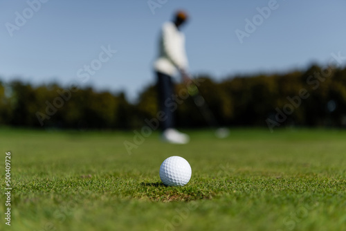 golf ball on fresh grass of green field near blurred man.