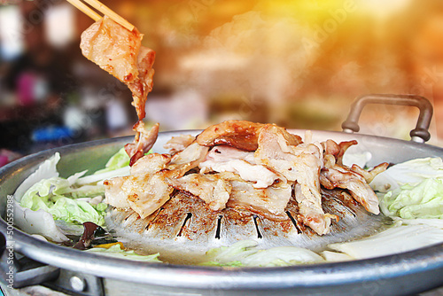 Hand hold chopsticks with Thai barbecue Grill Pork on hot pan buffet, vegetable and soup on hot pan, Moo Kra Ta (thai word) - Image