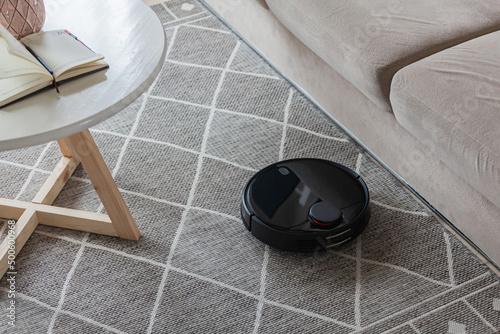 Robotic vacuum cleaner cleaning carpet at home next sofa