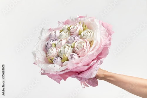 Delicate white-pink bouquet of marshmallows in hand on white background