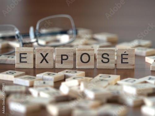 exposé word or concept represented by wooden letter tiles on a wooden table with glasses and a book