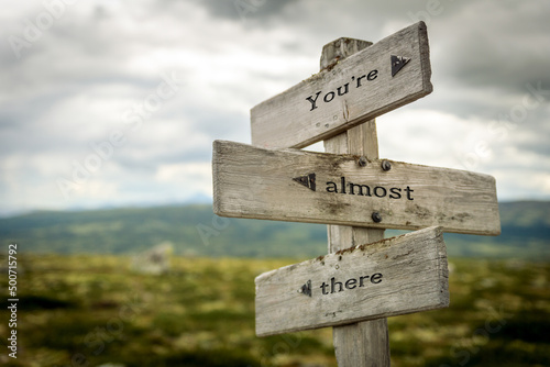 youre almost there text quote written in wooden signpost outdoors in nature. Moody theme feeling.