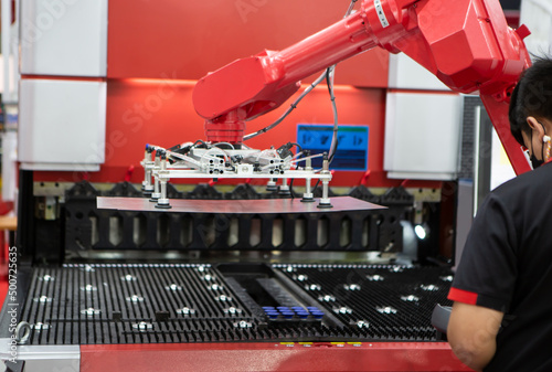 Robot arm loading metal sheet to laser cutting machine in production line. Industrial metalworking machinery.