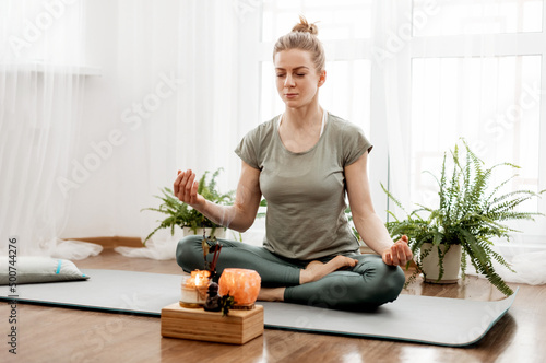 Young relaxed woman doing yoga at home with candles and incense