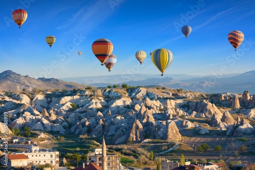 Colorful hot air balloons fly in blue sky over amazing rocky valley in Cappadocia, Turkey.