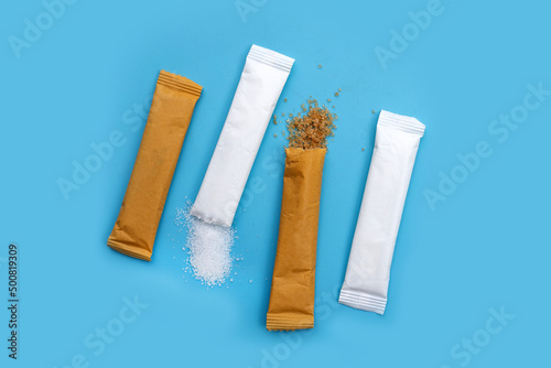White and brown sugar sachets on blue background.
