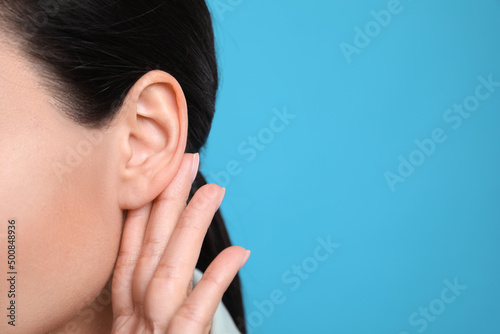 Woman showing hand to ear gesture on light blue background, closeup. Space for text