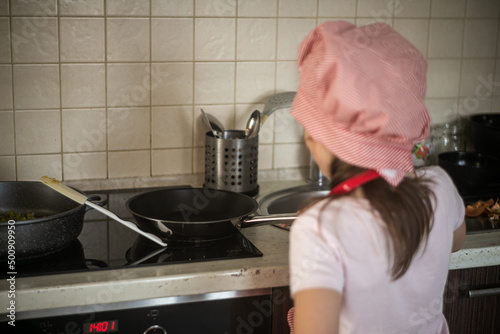 Dziewczynka stoi przed kuchenką i gotuje na patelni 