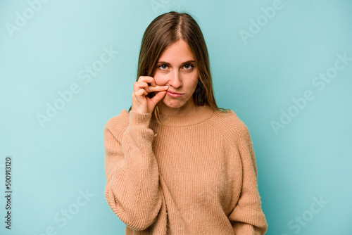 Young caucasian woman isolated on blue background with fingers on lips keeping a secret.