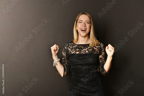 bellissima ragazza in abito di pizzo nero con mani sul viso in segno di felice sorpresa e vittoria