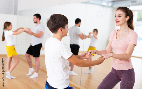 Positive pre-teen boy exercising dance moves with mother at family dance class while his father dancing with his sister