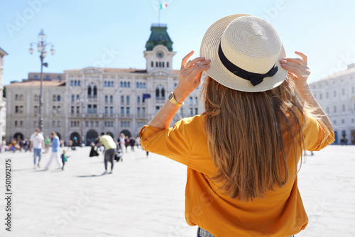 Tourism in Europe. Back view of pretty girl holding hat in Trieste, Italy. Beautiful young woman visiting Europe.