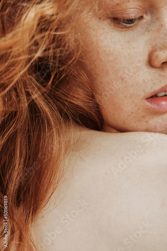 Close-up portrait of young woman with freckles on her face and red hair posing with shirtless back