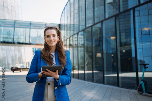 Successful woman real estate agent holding tablet and looking to camera. Business centre location.