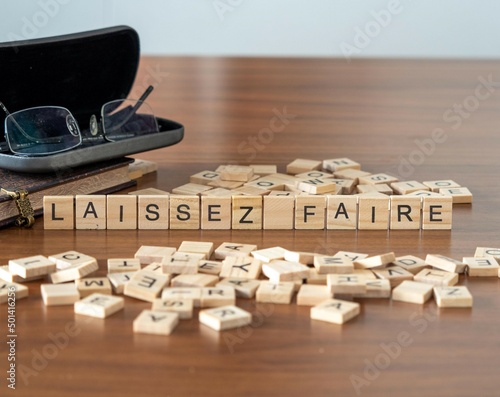 laissez faire word or concept represented by wooden letter tiles on a wooden table with glasses and a book