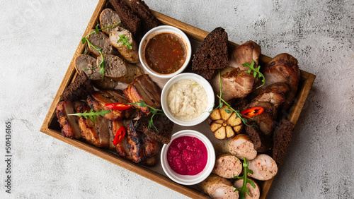 Close-up photo of mixed grilled meat platter. Beef, pork, poultry, sausages, grilled garlic, chili pepper, different sauces on marble background.