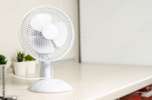 A small fan on the kitchen table. The concept of cooling and ventilation of the house. Copy space