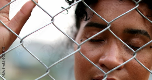 Sad African American woman looking through metal fence. South American person holding into fence