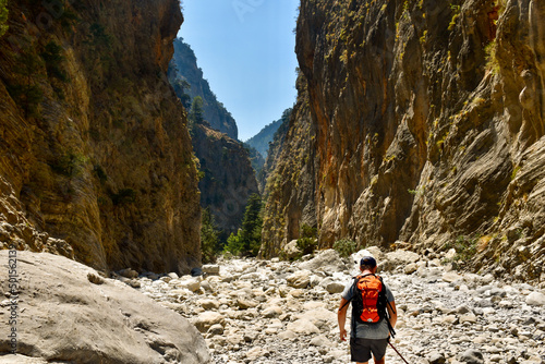 Man with orange backpack hiking in mountain valley by hot summertime in Samaria Gorge in Greece