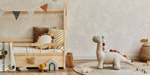 Stylish composition of cozy scandinavian child's room interior with wooden bed, pillows, plush dinosaur, wooden toys and textile decorations. Neutral wall, carpet on the floor. Copy space. Template.