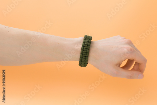 Man wearing a survival wristband on a hand on a yellow background. Bracelet. Elegance. Wrist. Tactical. Strong. Strap. Beauty. Knotted. Design. Survive. Emergency. Cord. Orange. Hold. Keep. Strength