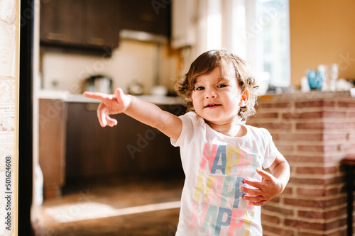 Funny toddler girl dancing indoors, little child play, baby having fun moving and jumping on the floor in a sunny white room, kitchen at home or kindergarten.