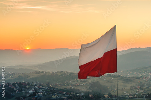 Biało-czerwona flaga Polski na tle zachodzącego słońca w górach - Ochodzita, Koniaków