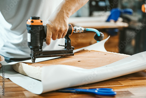 carpenter using nail gun or staple gun after replace a vinyl or upholstery fabric to the Seat for Bar Stools,furniture restoration woodworking concept. selective focus