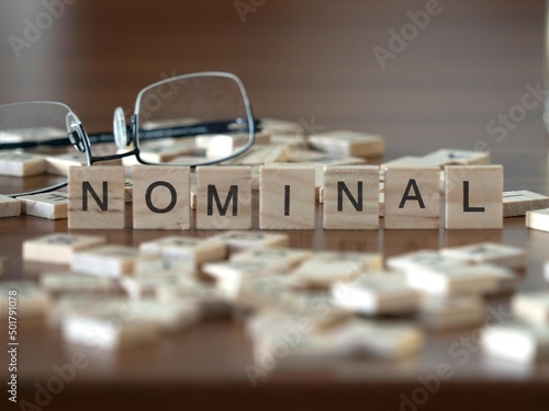 nominal word or concept represented by wooden letter tiles on a wooden table with glasses and a book