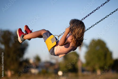 Little boy having fun on a swing on the playground in public park on summer day. Happy child enjoy swinging. Child playing on outdoor playground. Kids play on kindergarten yard.