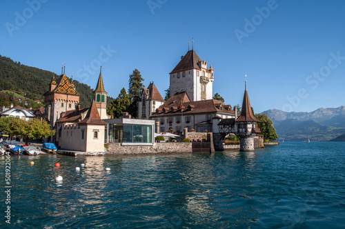 Oberhofen Castle in Switzerland - An old castle with lots of towers on the shores of the lake surrounded by mountains.