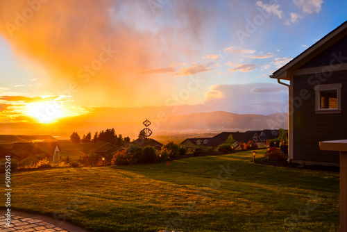 A colorful mist of rain covers the Spokane Valley as the sun reflects the sunset behind the mountains from a hilltop subdivision in Liberty Lake, Washington, USA.