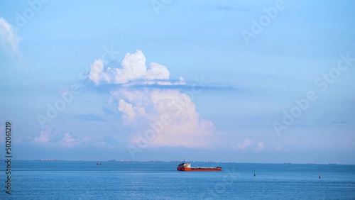 Breathtaking seascpe with a sailing red barge on blue cloudy sky on the background, water transport concept. Shot. Cargo ship barge on the sea horizon in a summer sunny day.