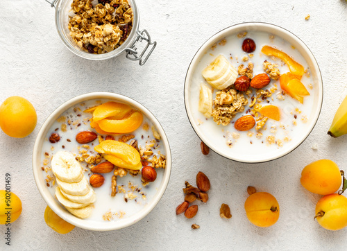 Healthy breakfast cereal top view. Granola breakfast with fruits, nuts, milk and peanut butter in bowl on a white background