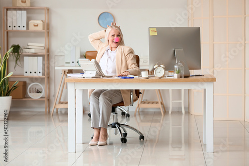 Funny mature woman with clown nose in office. April fools day celebration