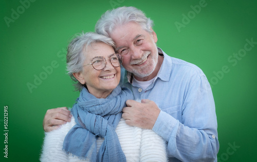Portrait of beautiful caucasian senior couple hugging with love smiling and looking at camera standing on green background