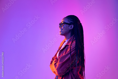 Profile view of young girl with afro hairdo in cotton shirt isolated on purple background in neon light. Concept of beauty, art, fashion, youth and emotions